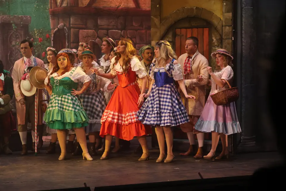 Villagers in green, red and blue gingham dresses strung across the stage in front of a painted street, straw hats and baskets among them.