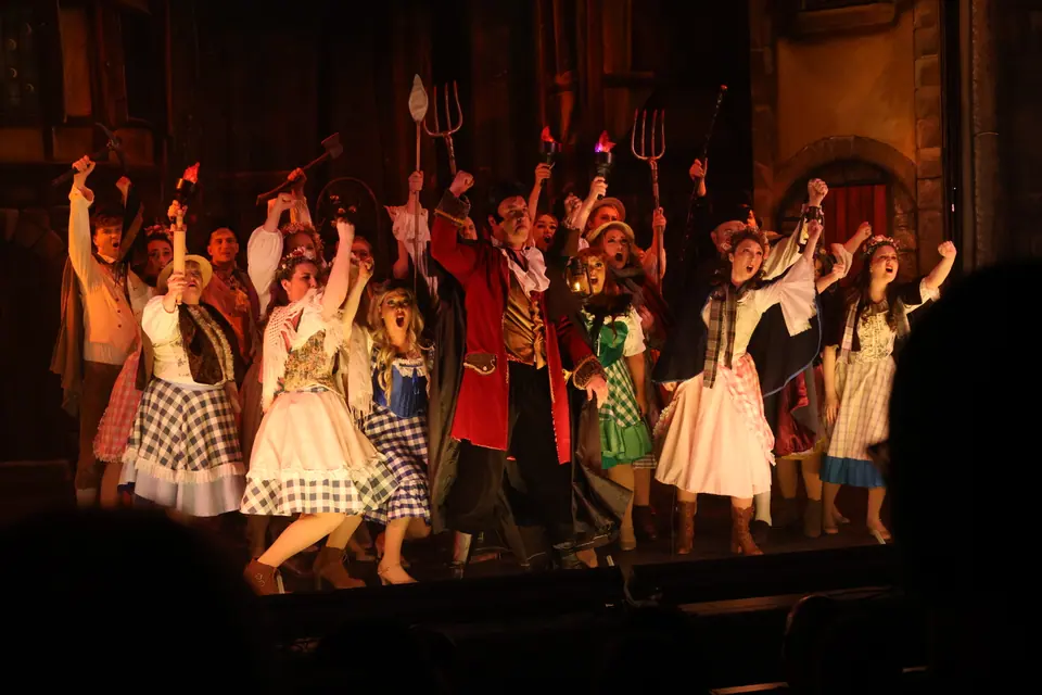 The company massed with torches, pitchforks and an axe raised overhead, a man in a red tailcoat at the centre, the light low and warm.