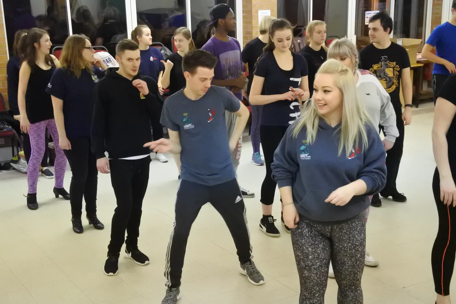 About a dozen members spread across the floor of a church hall, part way through a dance routine. Everyone is in tracksuits and trainers, and coats and bags are piled on chairs along the wall.