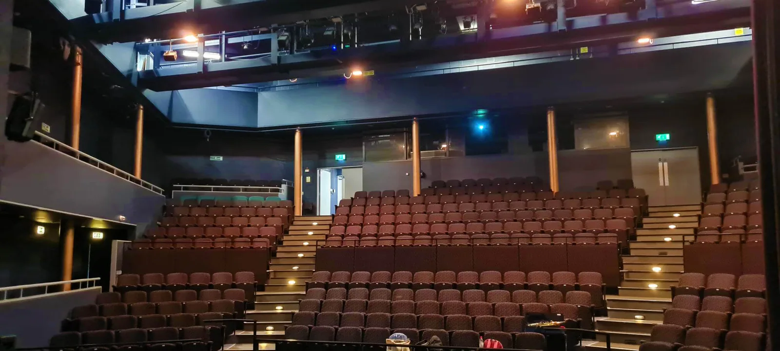 The auditorium at the Dormston Mill Theatre seen from the stage, with raked rows of seats in the stalls and a balcony running round above them.