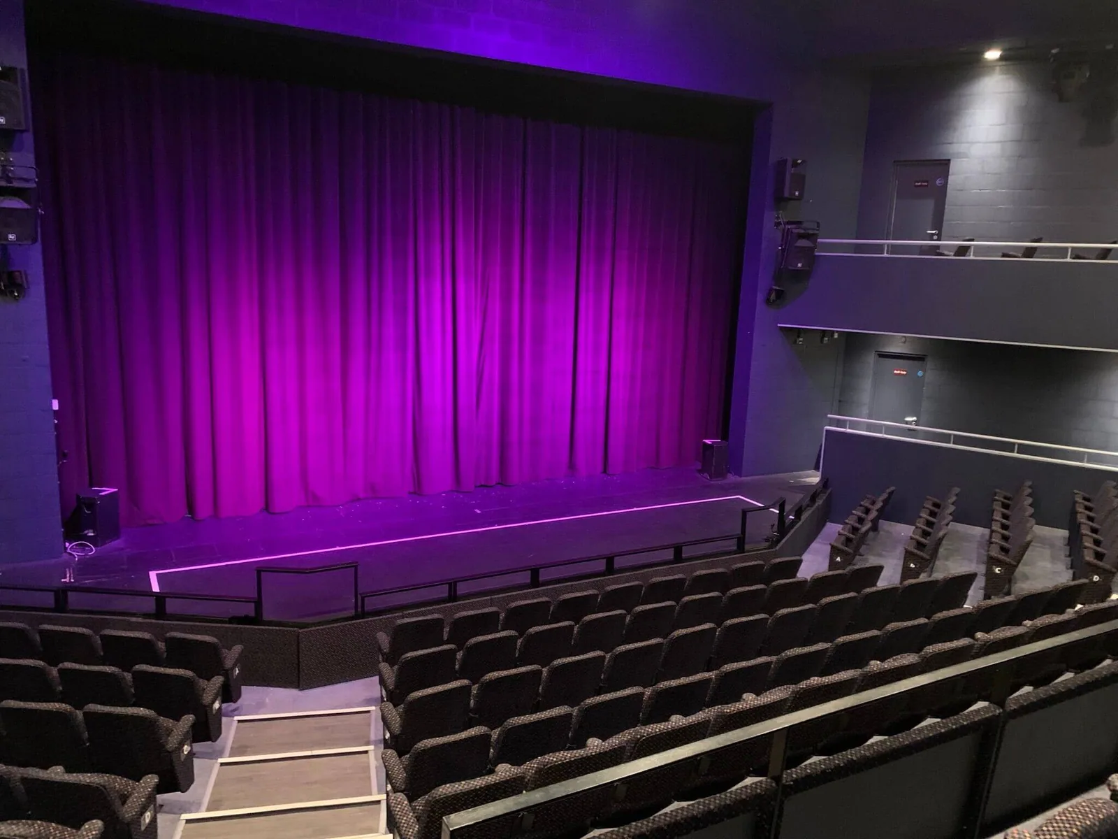 The stage at the Dormston Mill Theatre with the house tabs down and lit magenta, seen from the raked seating at the back of the stalls.